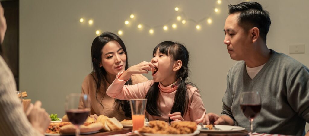 A family enjoys a meal together while lights hang behind them on a wall