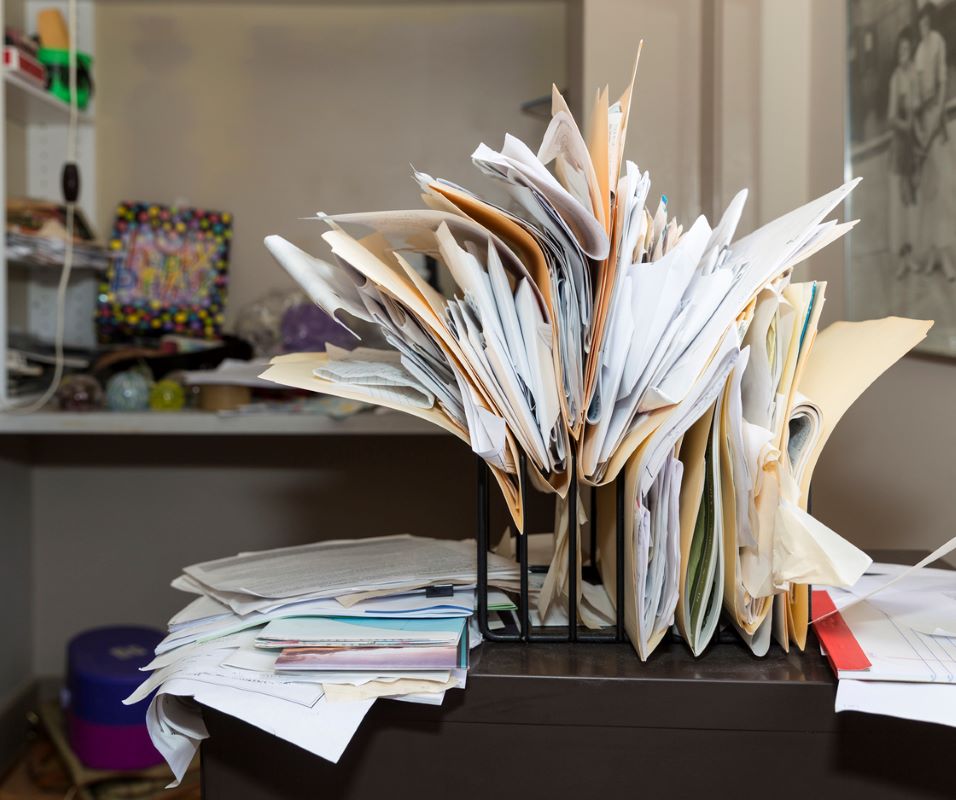 Cluttered desk with files and documents stored in an unorganized manner.
