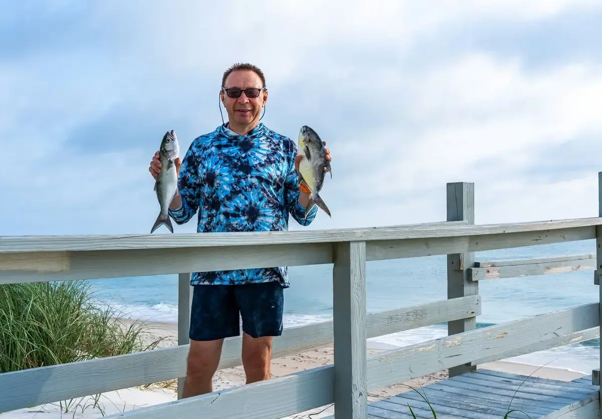 A man smiling as he holds up fish he’s recently caught.