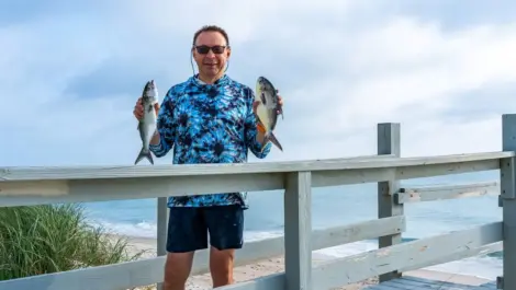 A man smiling as he holds up fish he’s recently caught.