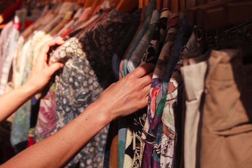 A person combs through vintage clothing hanging on a rack at a market. 