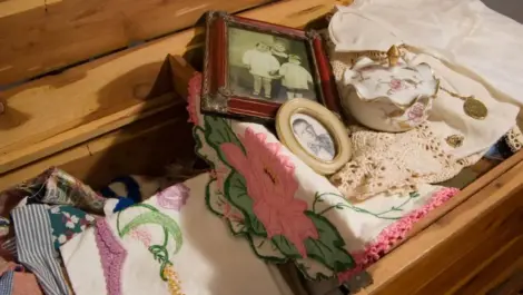 A view of a wooden storage bench holding family heirlooms, frames, and fabrics.