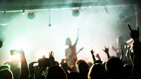 A crowd of people at a rock show raise their hands and enjoy the music from the band on stage.