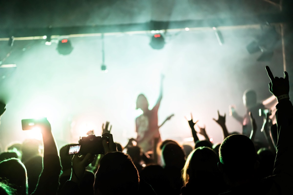 A crowd of people at a rock show raise their hands and enjoy the music from the band on stage.