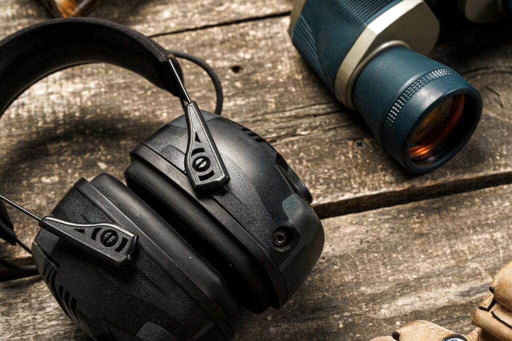 A close-up of protective headphones and binoculars on a wooden table.