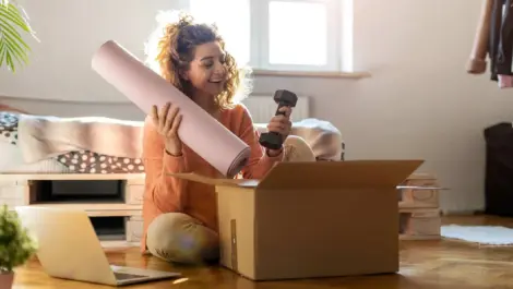 A woman smiles as she opens a package with a yoga mat and free weight.