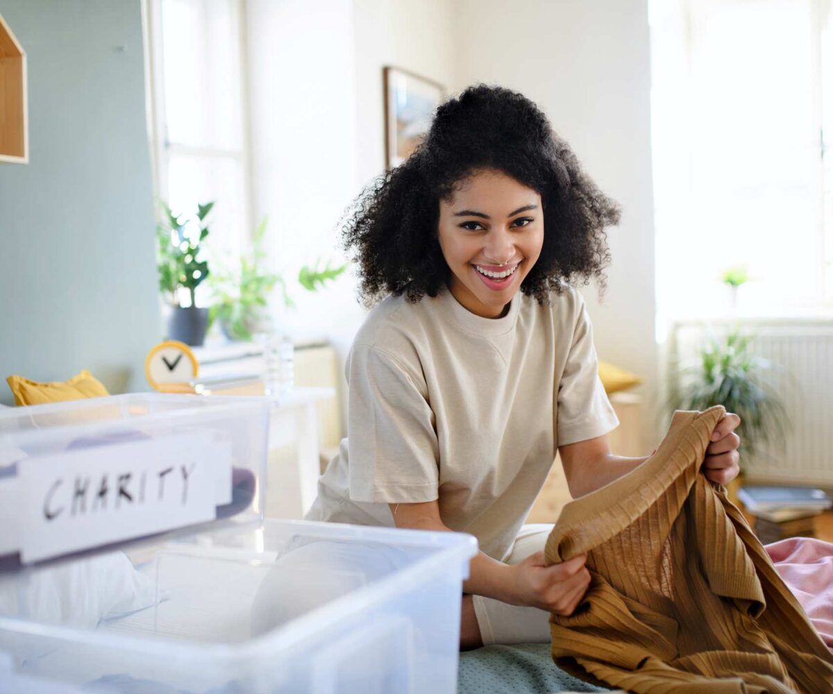 A happy woman sorts her clothing into bins to keep, donate, or throw away.