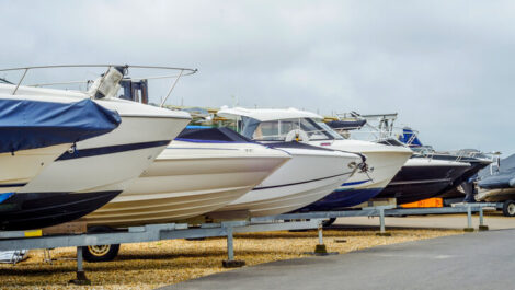 A row of covered boats on trailers stored together outdoors.