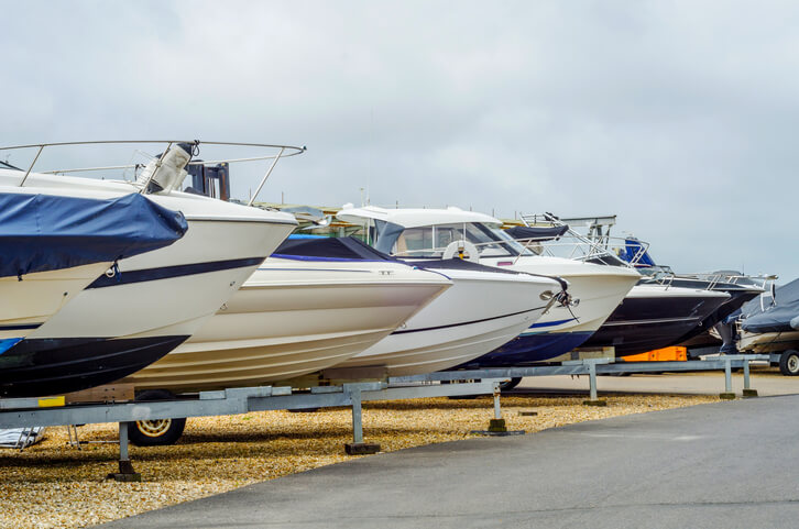 A row of covered boats on trailers stored together outdoors.