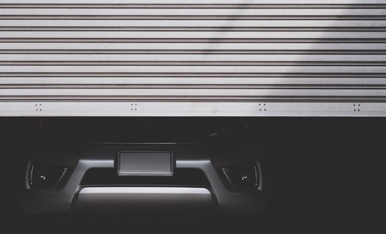 A half-open storage unit door with a silver SUV parked inside.