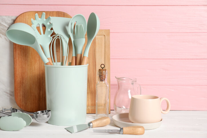 Essential kitchen tools in a mint green container in front of a pink background.