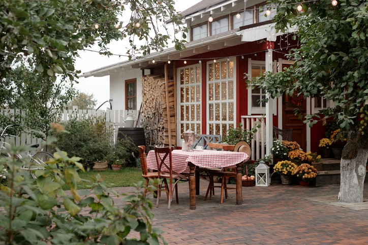 A patio beautifully decorated with string lights and plants, with a wooden table and chairs on brick pavers.