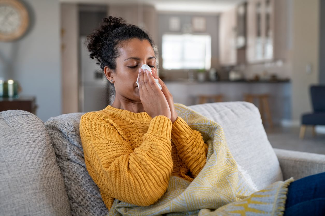 A woman on her couch blowing her nose after struggling with allergies
