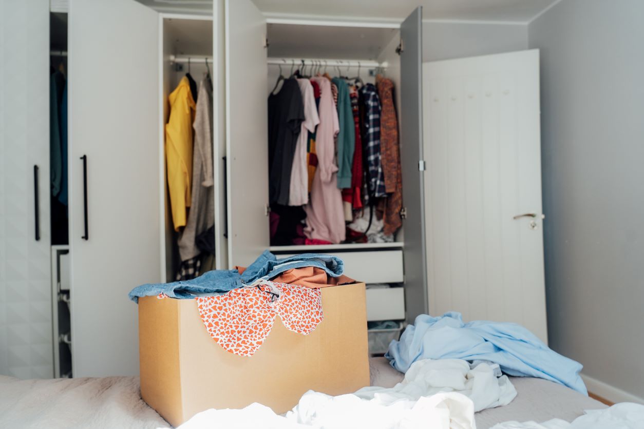 A room with a cardboard box full of clothes in front of an open closet.