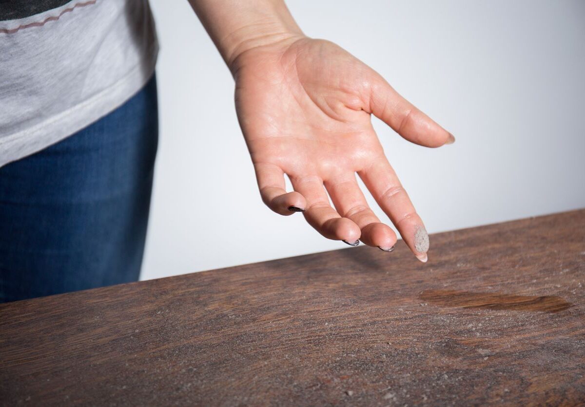 A hand with dust on the index finger after brushing it on a table